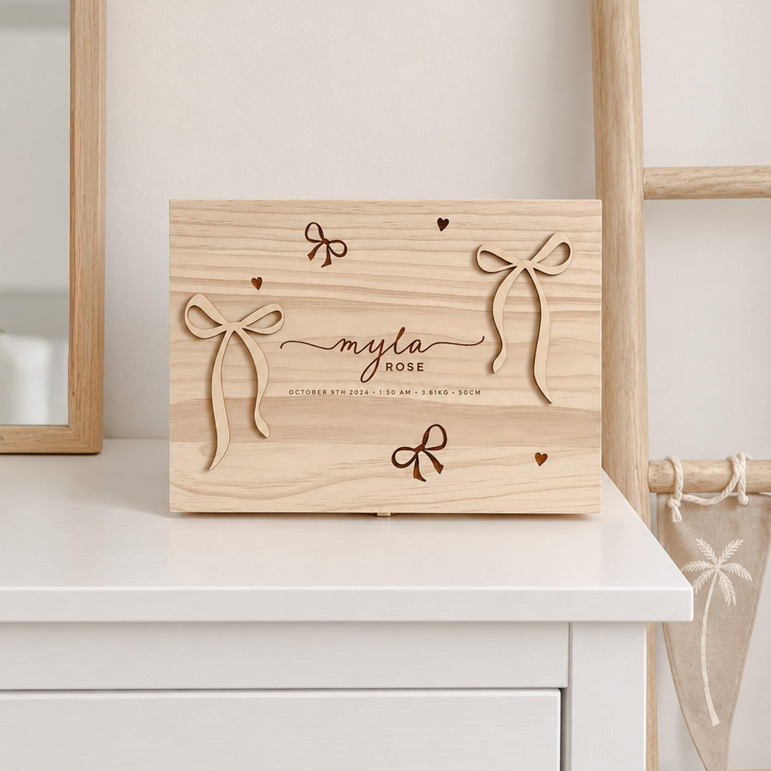 A personalized wooden keepsake box with laser-engraved bows and the name 'myla rose' on a white dresser, styled in a bright, modern room.