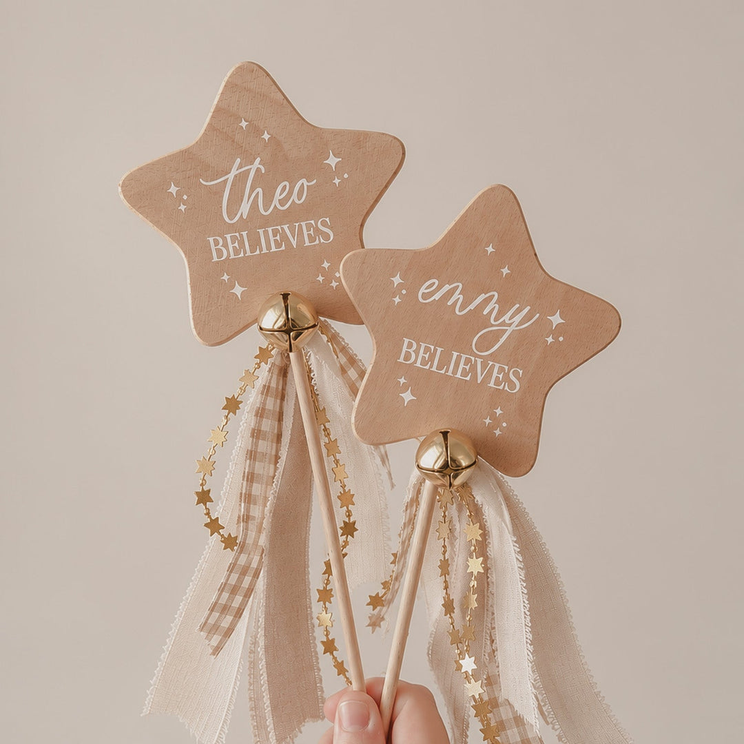 A hand holding two wooden star-shaped wand toppers with the words &