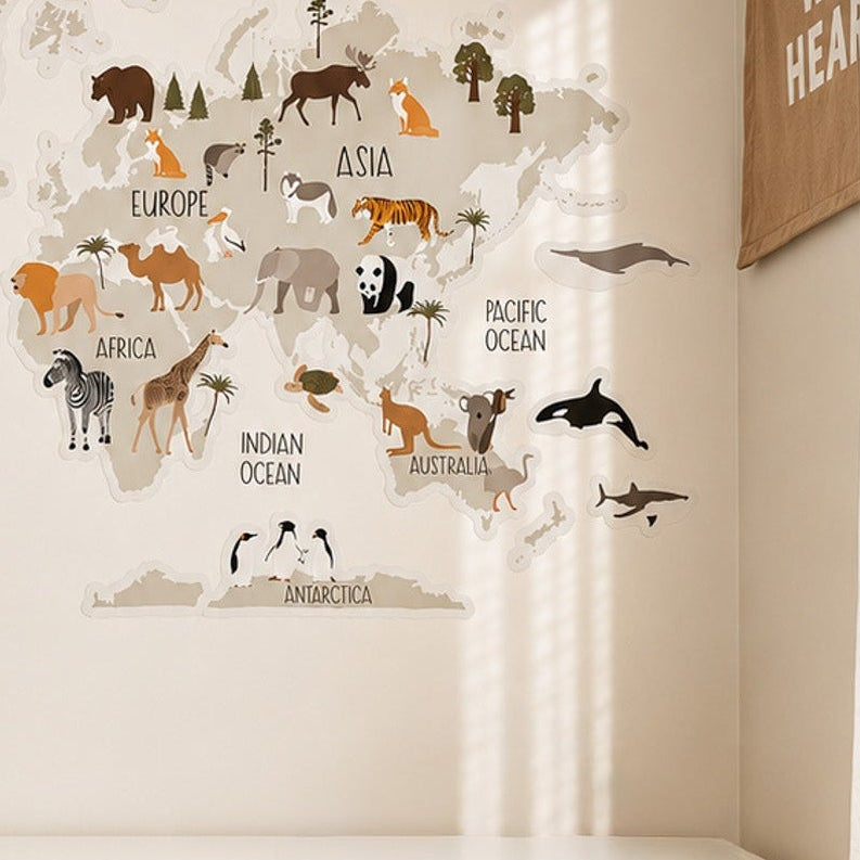A large animal-themed world map wall decal is displayed on a cream-colored wall above a white storage cabinet with woven baskets. The map features continents outlined in gray with various animals labeled by their ocean regions, set in a bright, modern nursery or playroom setting.