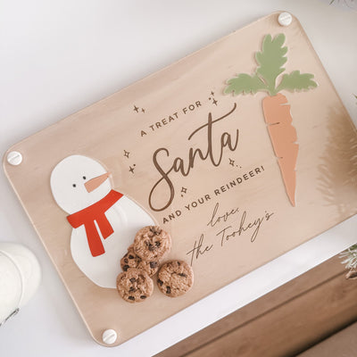 Decorative sign with a snowman, cookies, and text on a wooden surface.