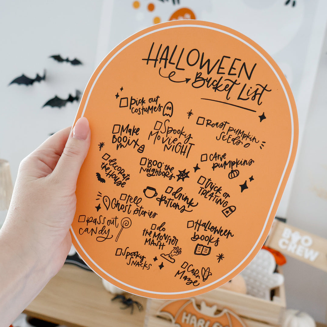 Halloween bucket list on a round board with festive decorations in the background
