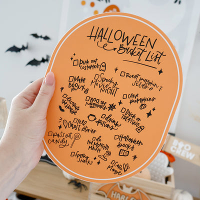 Halloween bucket list on a round board with festive decorations in the background