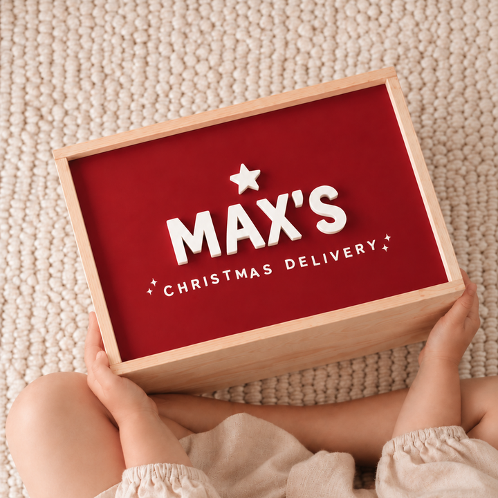 A child in a beige outfit holds a wooden box with a red insert printed with the words &